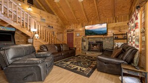 A cozy log cabin interior with a fireplace, leather sofas, a TV, and a staircase. - Easy Access, Outdoor Games, Open Skies (SEVIERVILLE)