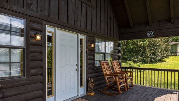 A log cabin with a wooden deck, a white door, and two rocking chairs. - Easy Access, Outdoor Games, Open Skies (SEVIERVILLE)