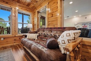 Interior de una cabaña de madera con un sofá de cuero, paredes de madera y ventanas grandes.