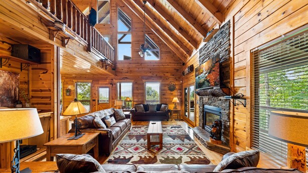 A log cabin interior with a wooden staircase, a fireplace, a sofa, and a dining table. - Outdoor Fireplace And Gorgeous Mountain Views (SEVIERVILLE)