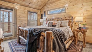 A wooden cabin bedroom with a large bed, wooden headboard, and a nightstand with a lamp. - Experience Exclusivity: Unwind at Moonrise Pool Lodge Luxury Cabin (SEVIERVILLE)