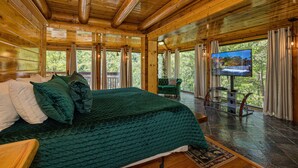 Ein geräumiges Schlafzimmer mit einem großen Bett, Holzbalkendecke, Fernseher und Blick ins Freie.