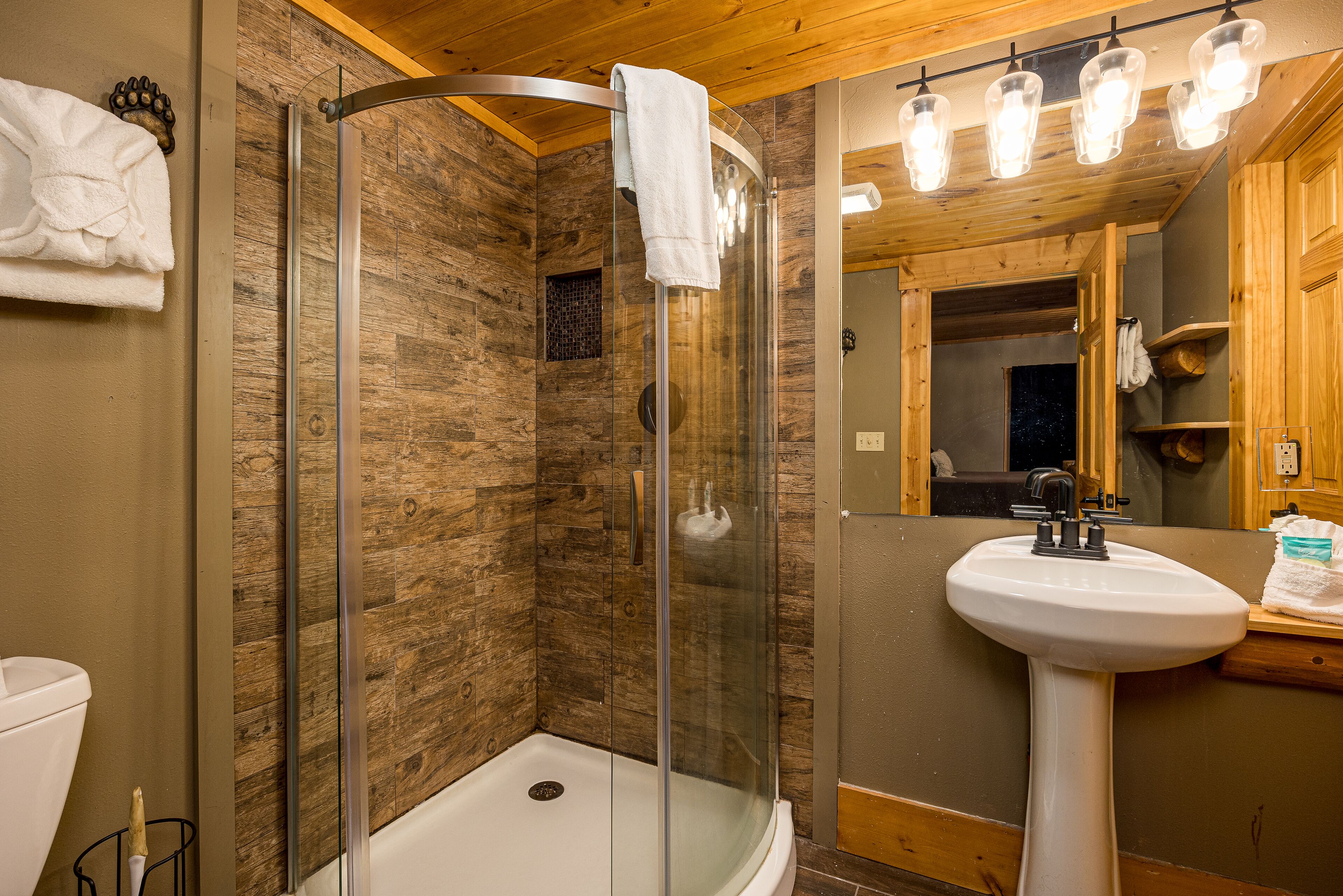 A bathroom with a glass-enclosed shower, a white sink, and wooden paneling.
