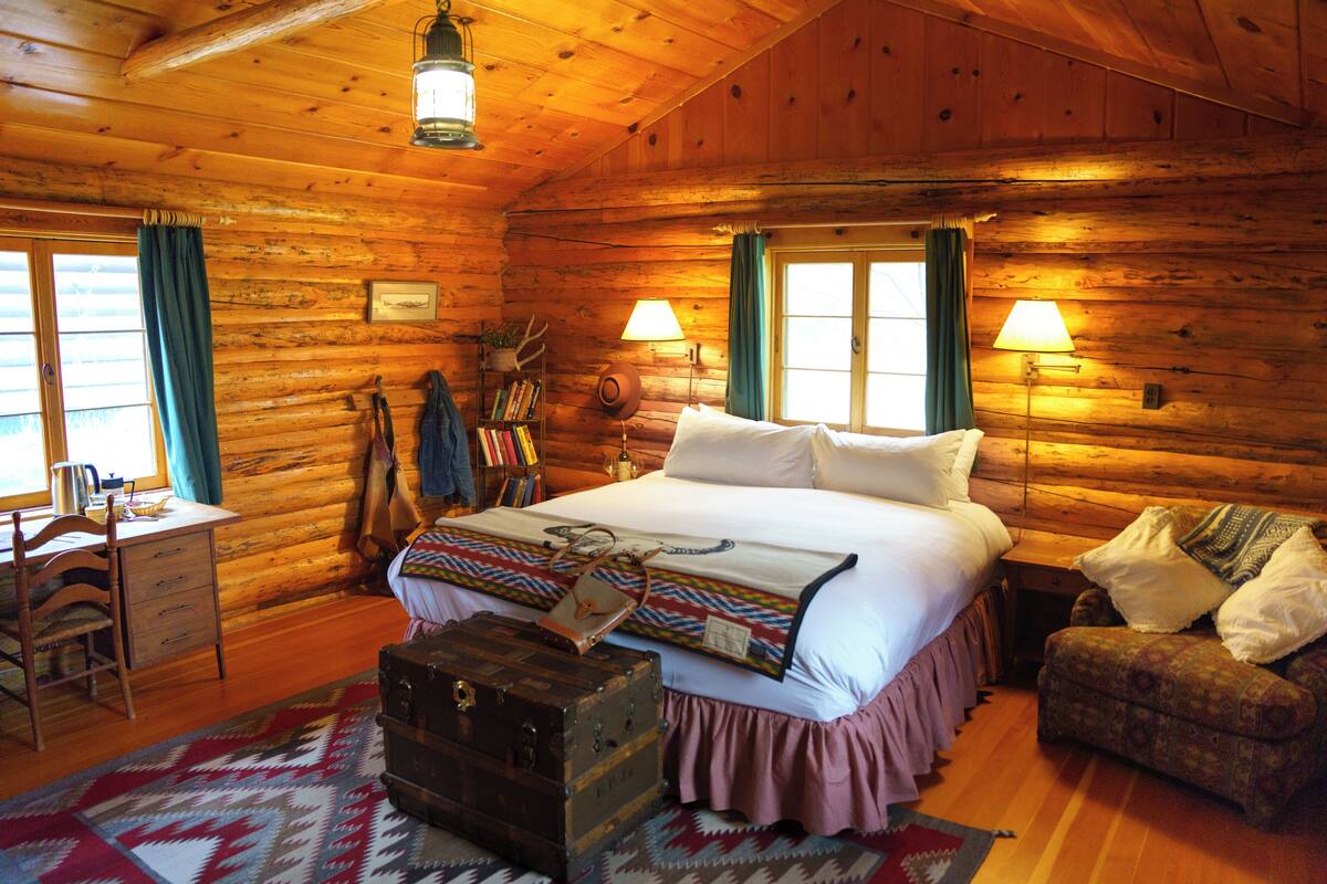 A log cabin bedroom with a bed, dresser, chair, and a suitcase.