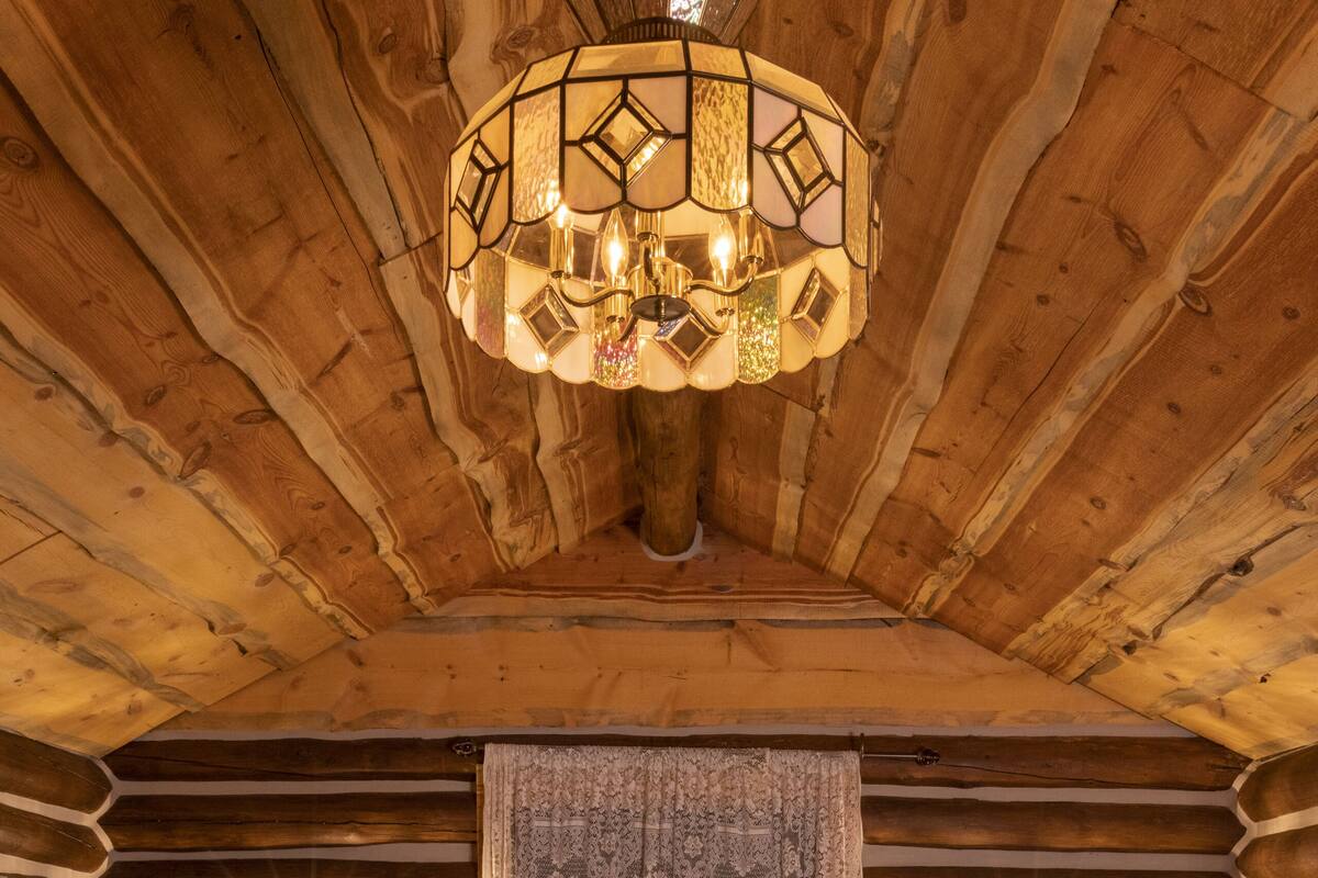 A log cabin bedroom with a bed, two wall-mounted lamps, a patterned curtain, and a hanging light fixture.