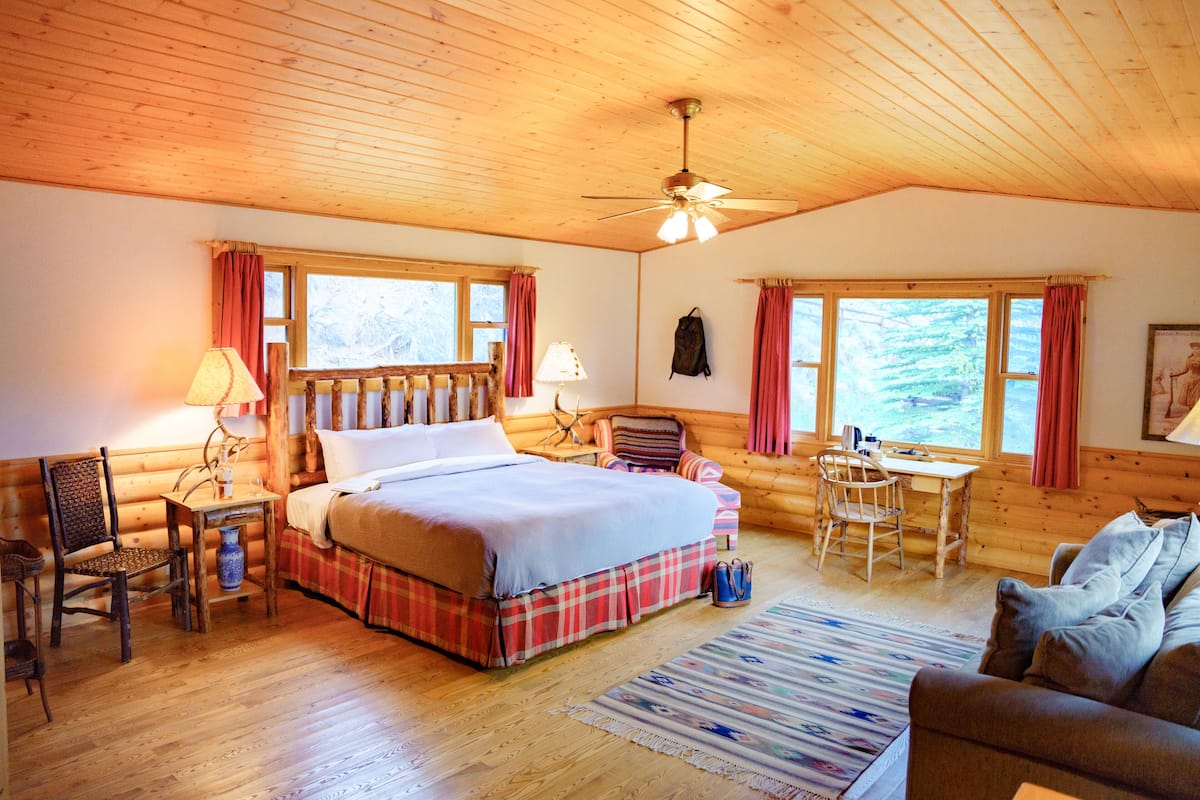 A cozy log cabin bedroom with a large bed, a desk, and a chair.