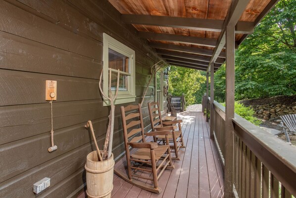 A wooden porch with rocking chairs, a wooden bucket, and a wooden door with a window. - Screened In Hot Tubs Bring Joy All Year Round (GATLINBURG)