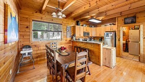 A wooden cabin interior with a dining area, kitchen, and a window providing a view of the outdoors. - 1 Awesome View - Secluded Cabin In Pigeon Forge (PIGEON FORGE)