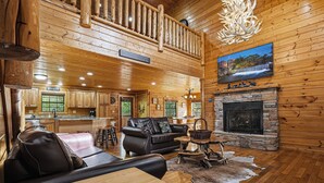 A log cabin interior with a fireplace, leather sofa, dining area, and a view of the outdoors. - 3 Crazy Cubs-Close to Pigeon Forge and Dollywood (SEVIERVILLE)
