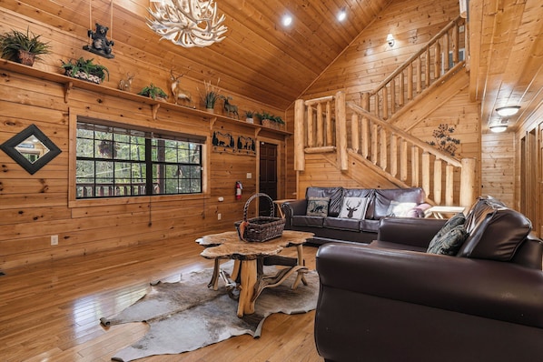 Interior de madera con una escalera, un sofá, una mesa y objetos decorativos.