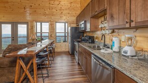 A wooden cabin kitchen with a long dining table, bar stools, a refrigerator, microwave, and a blender. - 4 States View-Gatlinburg, Private Pool, Game Room (GATLINBURG)