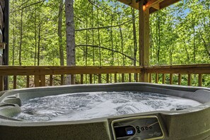A hot tub with a digital temperature display, surrounded by a wooden deck and a forest backdrop. - Authentic Log Cabin close to Pigeon Forge*Fire Pit*Hot Tub (PIGEON FORGE)