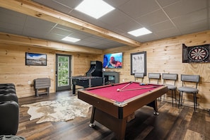A pool table, foosball table, dartboard, and bar stools in a wooden room with a leather rug. - Authentic Log Cabin close to Pigeon Forge*Fire Pit*Hot Tub (PIGEON FORGE)