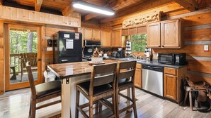 Cocina de cabaña de madera con una mesa de comedor, sillas, un refrigerador, un microondas y una cafetera.