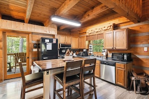 A wooden cabin kitchen with a dining table, chairs, a refrigerator, a microwave, and a coffee maker. - Authentic Log Cabin close to Pigeon Forge*Fire Pit*Hot Tub (PIGEON FORGE)