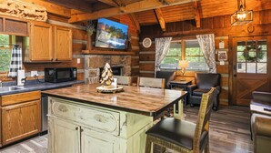 Interior rústico de una cabaña con una mesa de madera, un televisor en la pared y una chimenea.