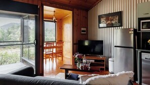 A cozy cabin interior with a wooden ceiling, a dining area, a TV, and a refrigerator.