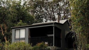A modern, two-story house with a dark exterior, large windows, and a covered porch area.