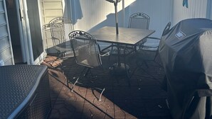 Une terrasse avec une table et des chaises, un barbecue abrité et un parasol.
