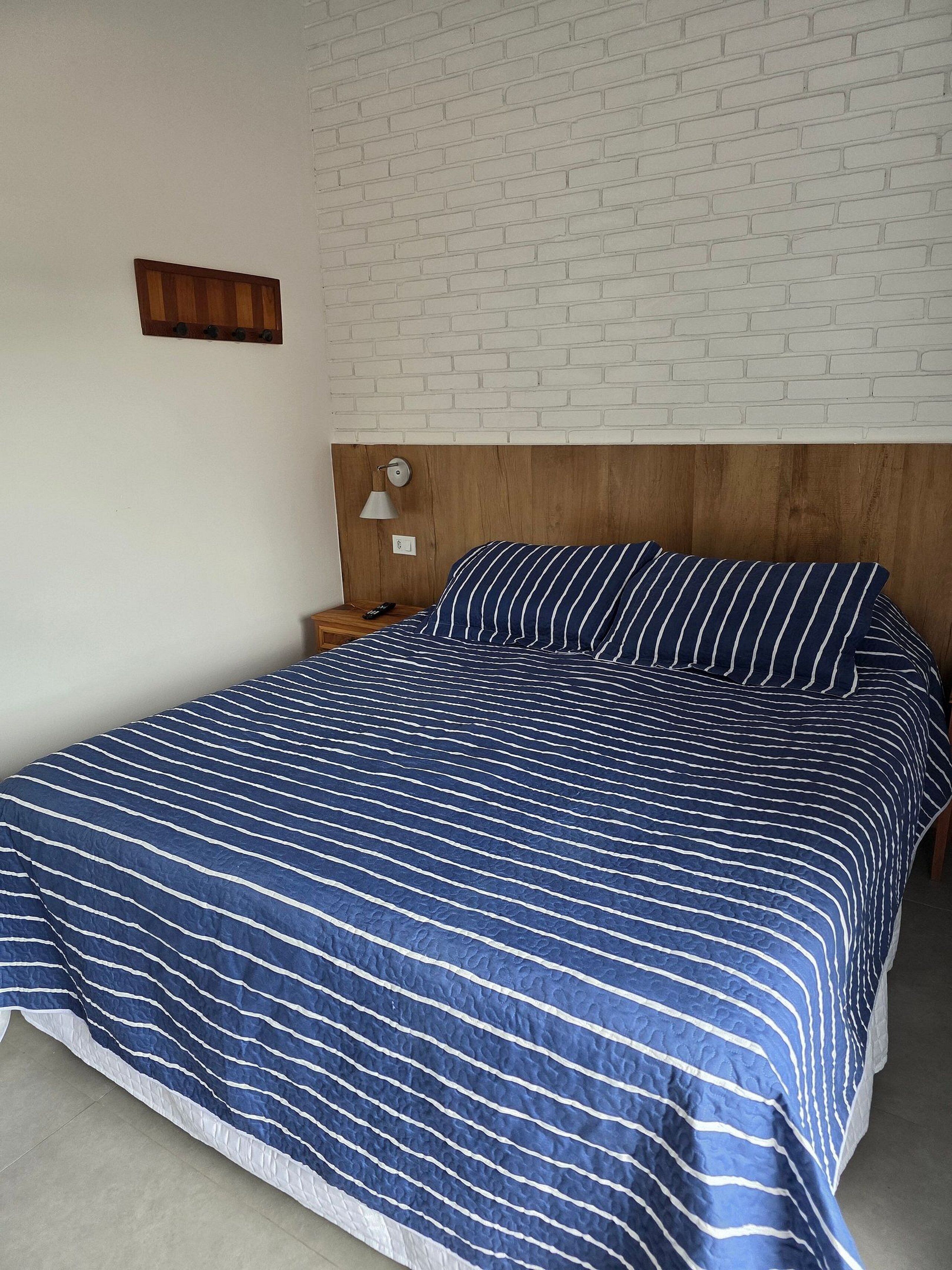A bedroom with a bed, a nightstand, a lamp, and a brick-patterned wall.