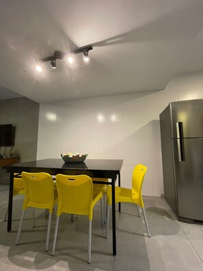 A modern kitchen with a dining table, four yellow chairs, a stainless steel refrigerator, and recessed ceiling lights. - Chalé 5 (Ubatuba)