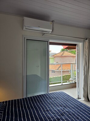 A bedroom with a bed, a sliding glass door leading to a balcony, and an air conditioning unit on the wall. - Chalé 5 (Ubatuba)
