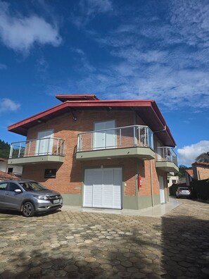 A two-story building with a red roof, a garage door, and a balcony with a metal railing. - Chalé 5 (Ubatuba)