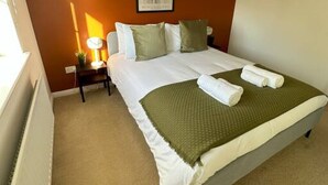 A neatly arranged bedroom with a bed, pillows, a bedside lamp, and a framed artwork on the wall.