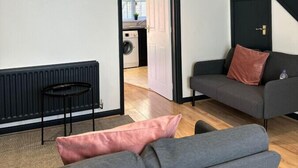 A modern living room with a grey sofa, a black radiator, and a staircase leading to another level.