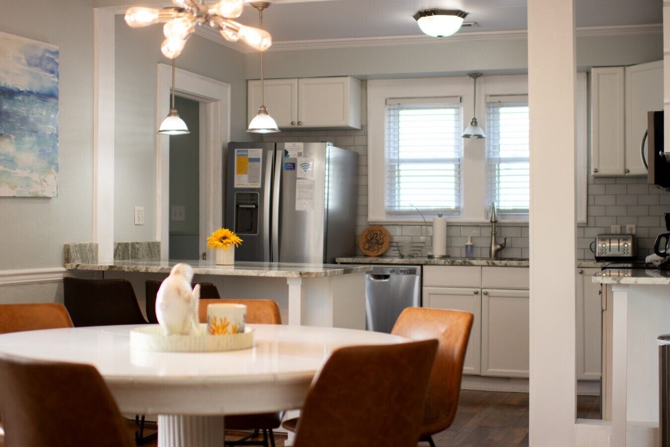 A modern kitchen with white cabinets, stainless steel appliances, and a dining area with a round table and chairs.