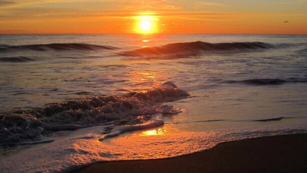 Een zonsondergang boven de oceaan, met golven die de kust naderen.