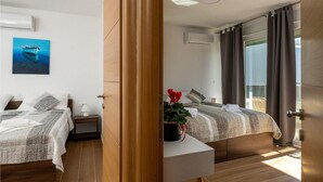 A modern hotel room with two beds, a large window with curtains, a ceiling fan, and a painting of a boat on the wall. - 2 bedroom nice home in Vodnjan (Vodnjan)