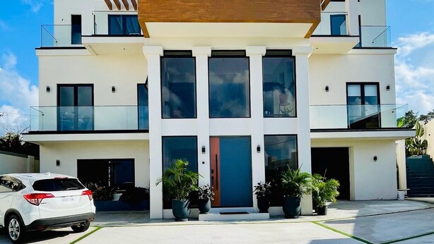Un bâtiment moderne à deux étages, doté d’une entrée centrale, de grandes fenêtres et d’un espace de stationnement où se trouve une voiture blanche.