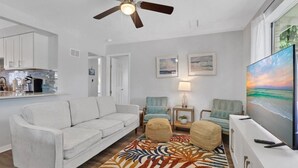 A living room with a sofa, two armchairs, a coffee table, a TV, and a ceiling fan.