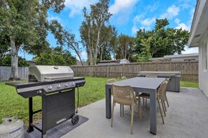 Un patio exterior con una parrilla, mesa y sillas.