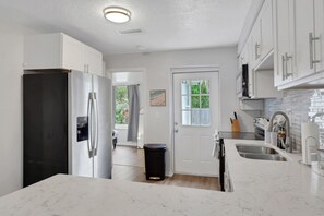 A modern kitchen with white cabinetry, a black refrigerator, a marble countertop, and a window with a view of greenery. - Fenced in w/ Jacuzzi Close to Siesta Key Bridge (Sarasota)