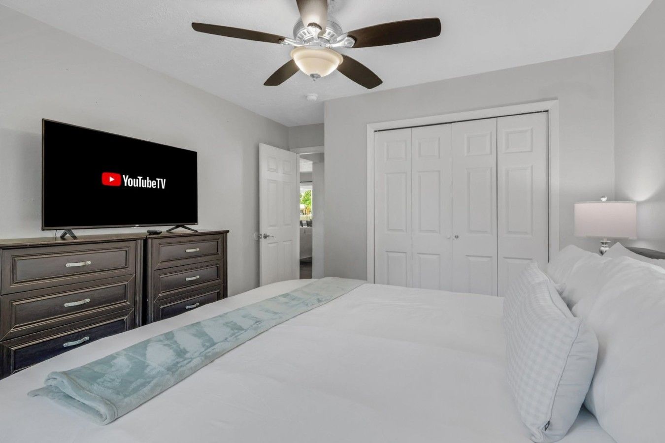 A bedroom with a bed, a TV on a dresser, a ceiling fan, and a door.