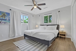 A bedroom with a bed, two bedside tables, a ceiling fan, and a window with curtains.