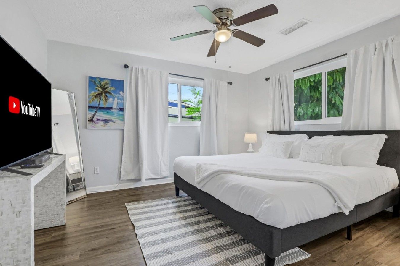 A modern bedroom with a bed, a ceiling fan, a TV, and a window with curtains.