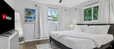 A modern bedroom with a bed, a ceiling fan, a TV, and a window with curtains.