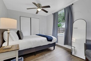 A bedroom with a bed, bedside table, lamp, ceiling fan, window with curtains, and a view of the outdoors. - Fenced in w/ Jacuzzi Close to Siesta Key Bridge (Sarasota)