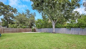 A backyard with a wooden fence, a tree, and a grassy lawn.