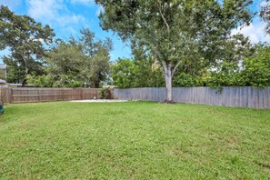 A backyard with a wooden fence, a tree, and a grassy lawn. - Fenced in w/ Jacuzzi Close to Siesta Key Bridge (Sarasota)