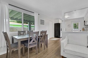 A dining area with a table and chairs, a white sofa, and a kitchen area with a refrigerator.