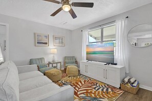 A living room with a sofa, chairs, a television, a ceiling fan, a window with curtains, and a rug. - Fenced in w/ Jacuzzi Close to Siesta Key Bridge (Sarasota)