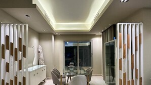 A modern dining area with a glass table and chairs, a white cabinet, and a view through a glass door. - Villa With Private Pool In Beverly Hills comp -Allegria residence-Sheikh Zayed (Giza Governorate)