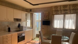 A modern kitchen with white cabinets, a microwave, and an oven. There is a dining area with a glass table and white chairs. - Azul y mar (Las Palmas de Gran Canaria)