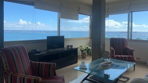 A spacious living room with a large glass table, striped armchairs, a black entertainment unit, and a view of the sea. - Azul y mar (Las Palmas de Gran Canaria)