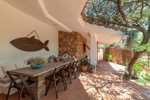A stone wall, a wooden table, and chairs in a shaded outdoor area. - Villa 'Gabbiani' with Sea View, Wi-Fi and Air Conditioning (Portobello)