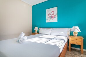 Un lit bien fait, avec du linge de lit blanc, un mur d’accent de couleur turquoise, une œuvre d’art florale et des lampes de chevet.
